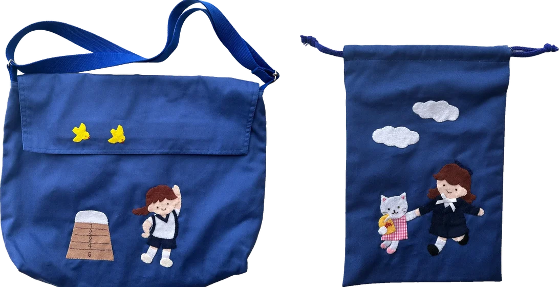 跳び箱と体操服の女の子のワッペンを付けた青いショルダーバッグと、制服の女の子とねこのワッペンを付けた紺のシューズバッグ